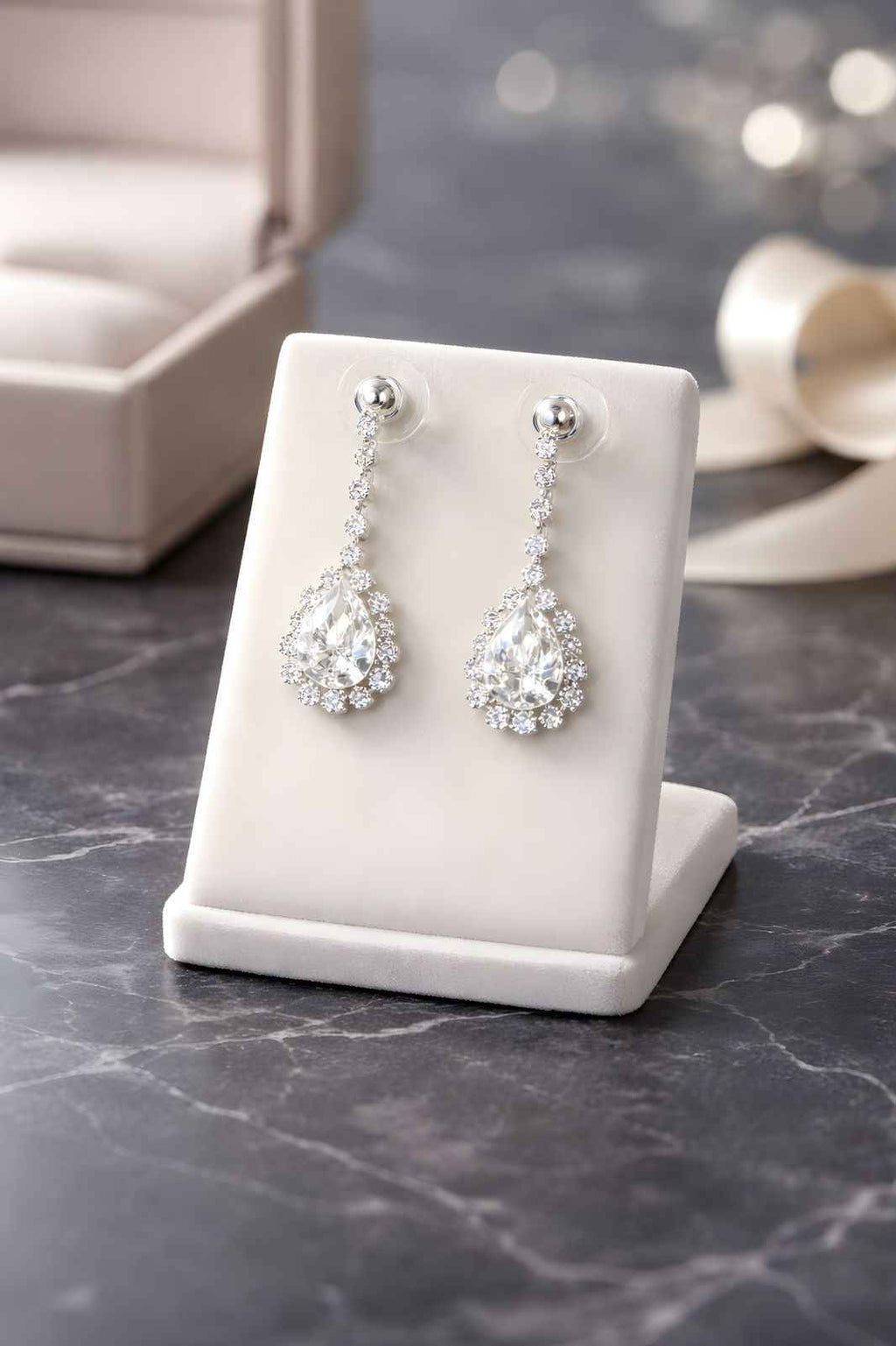 Teardrop drop earrings with clear stones on white jewelry stand
