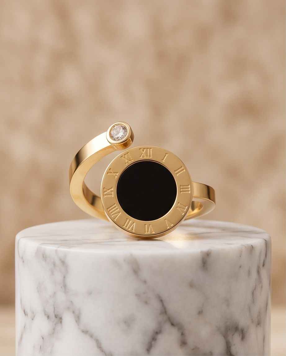 Gold Roman numeral ring with black face and small clear stone, displayed on marble