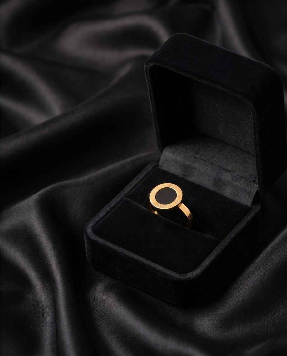 Gold Roman numeral ring with black round center stone in open black jewelry box