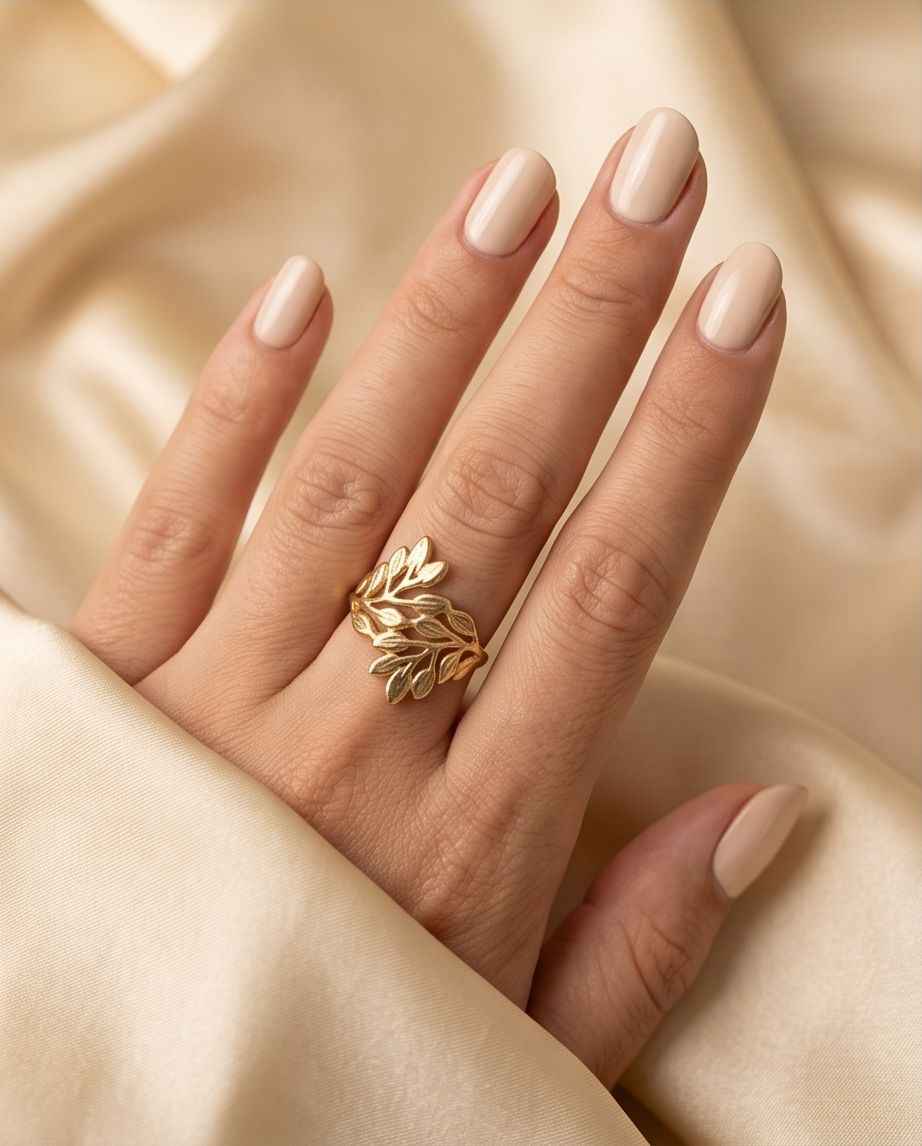 Gold-tone leaf statement ring on a hand with nude nail polish