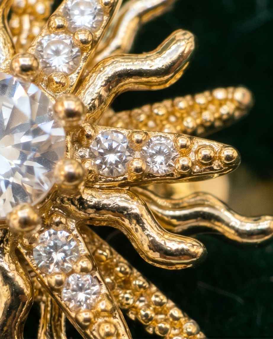 Gold statement ring with ornate starburst design and clear gemstone accents, close-up