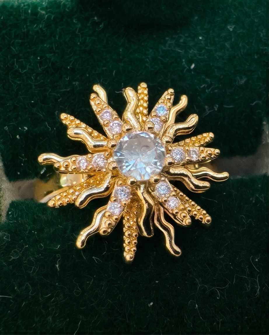 Gold starburst statement ring with central round clear stone and small sparkle accents