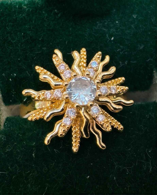 Gold starburst statement ring with central round clear stone and small sparkle accents