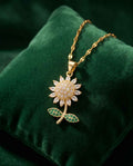 Gold-tone necklace with round sun pendant, clear stones, and green leaf accents