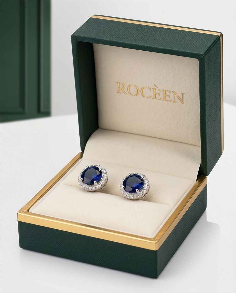 Pair of sapphire halo stud earrings in open gift box with blue center and crystal halo