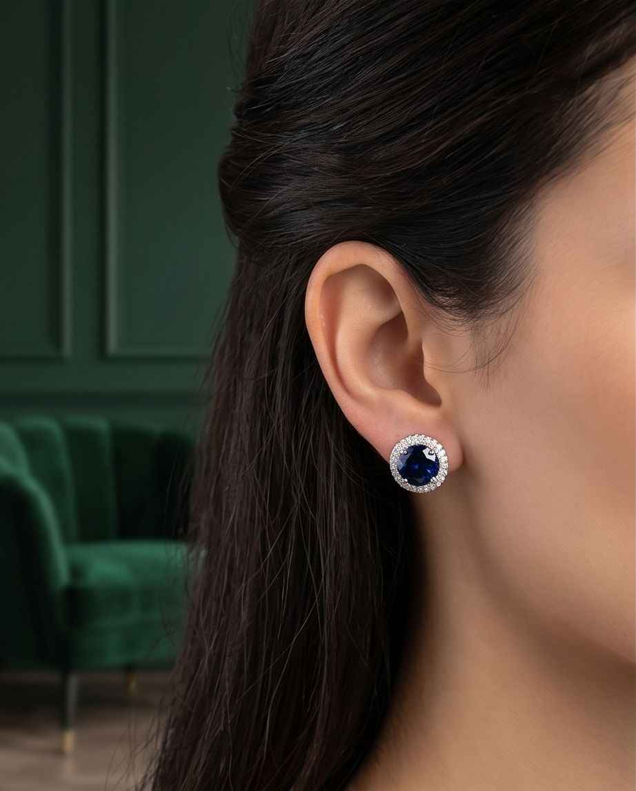 Sapphire halo stud earrings on ear with blue center stone and crystal halo