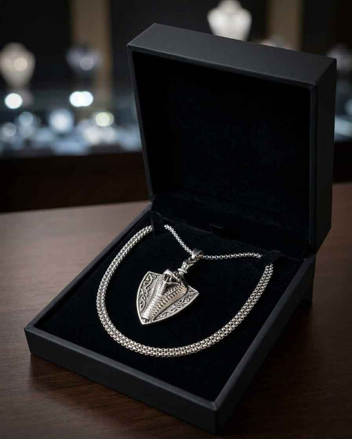Silver-tone shield charm necklace with layered chain on black display
