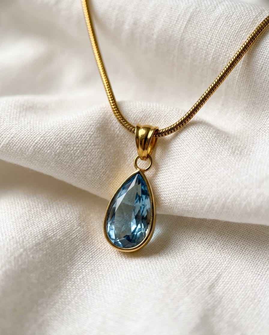 Gold chain necklace with blue teardrop pendant and oval bail
