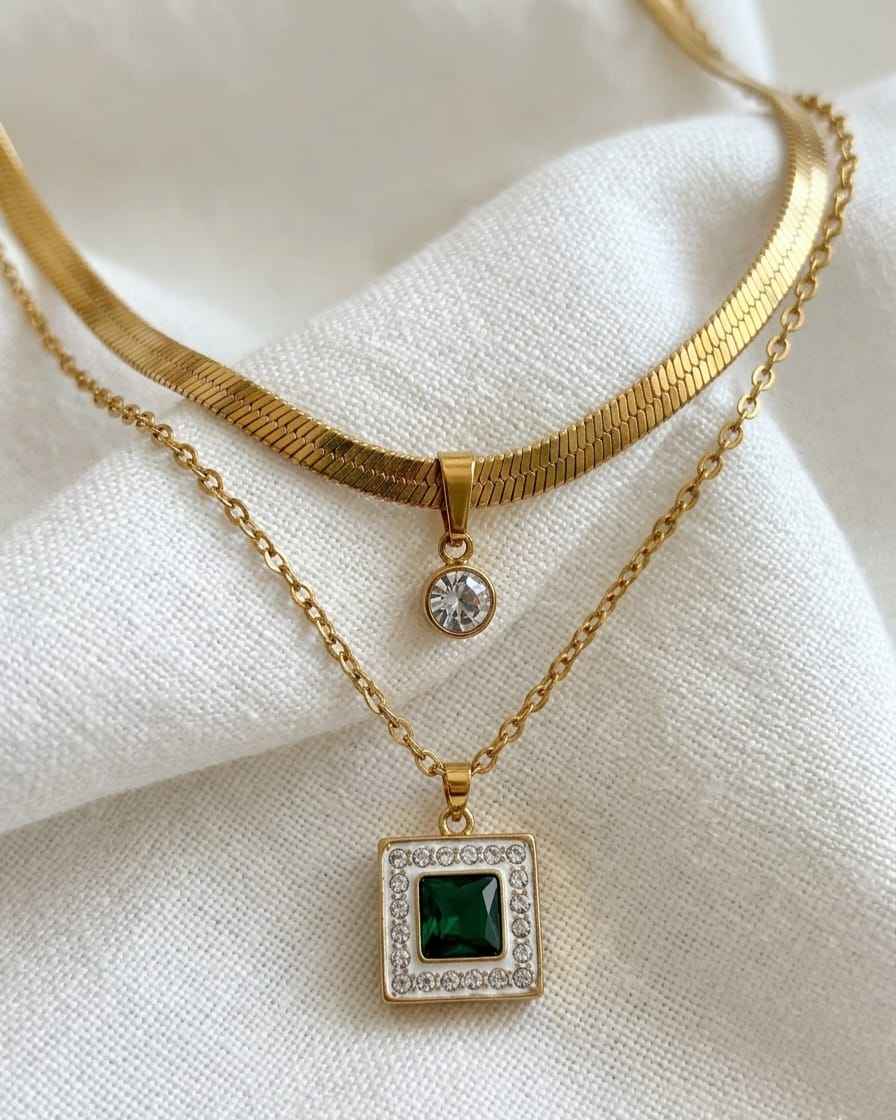 Layered gold-tone necklaces with round crystal top charm and square pendant with dark center