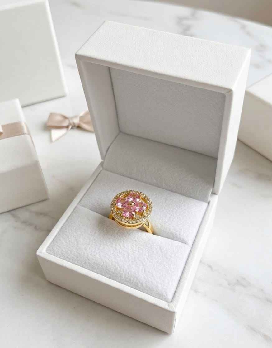 Gold halo ring with pink center stones, displayed in open white jewelry box