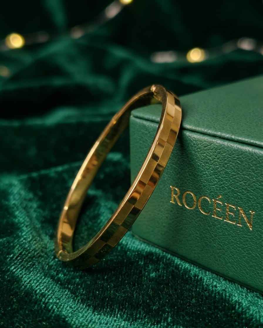 Gold faceted bangle bracelet with slim checker-pattern metal links on surface.