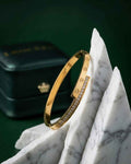 Gold bangle with screw motif and pavé stone inlay along the outer edge