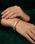 Gold-tone pavé link bangle with crystal-like stones and round emblem detail