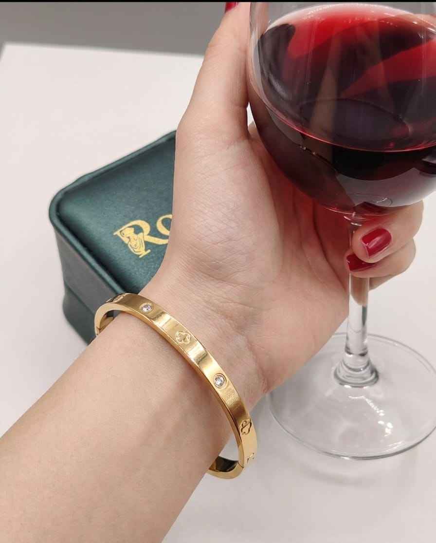 Gold bangle on wrist with bezel-set crystals and engraved pattern along the band