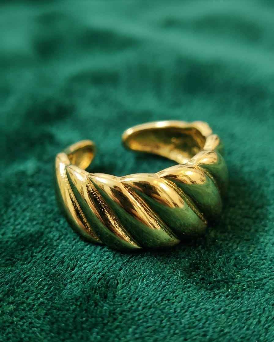 Gold sculpted cuff ring with twisted ridged wave pattern on textured green fabric