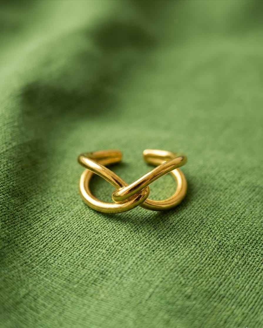 Gold intertwined open ring, two bent bands crossing at center on green fabric