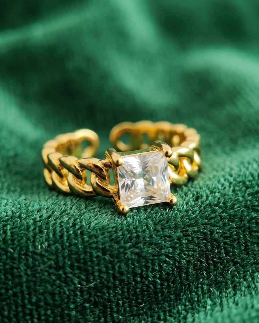 Gold-tone chain solitaire ring with clear square center stone on green fabric