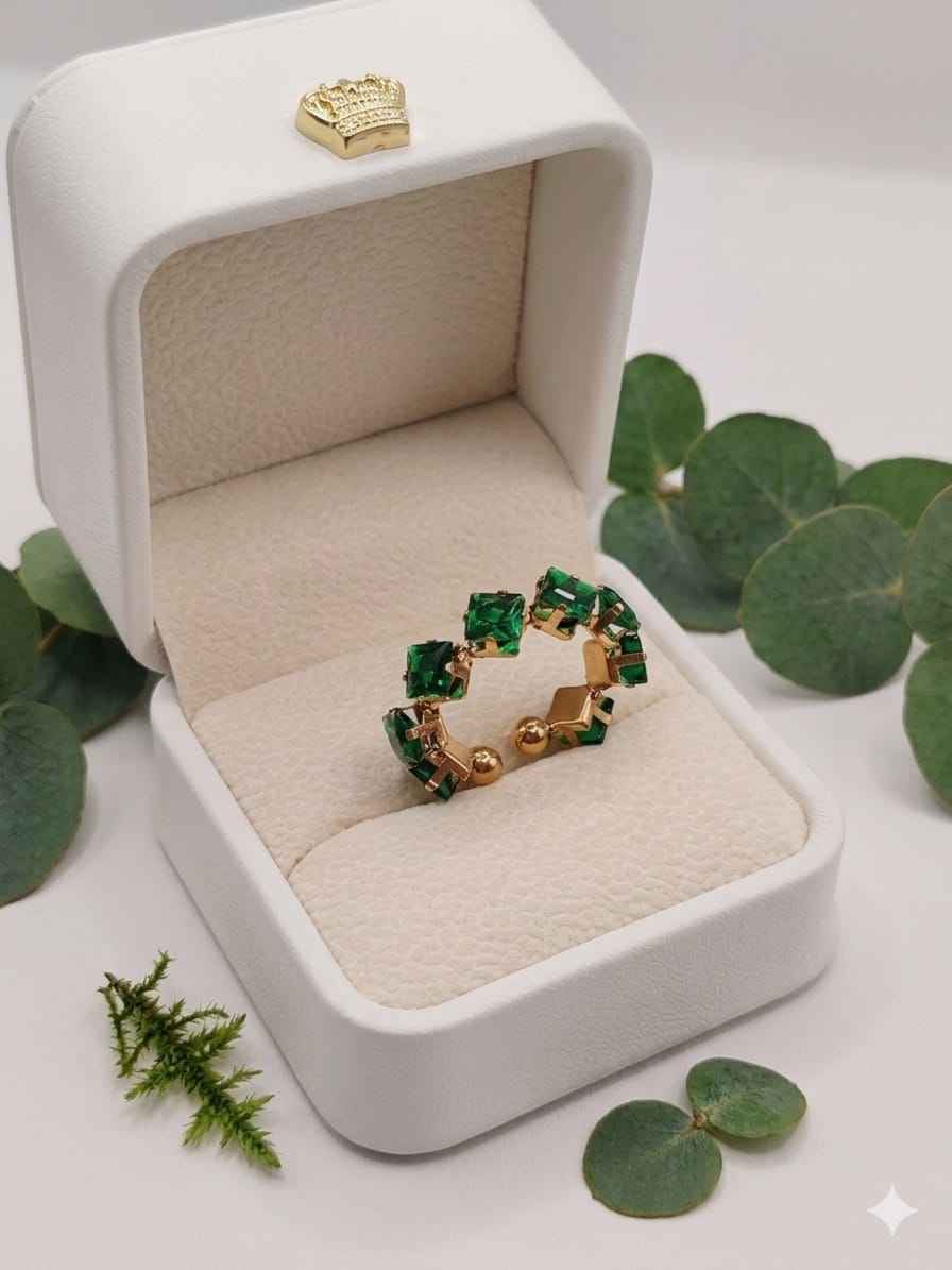 Open band ring with green stones in gold-tone settings in a jewelry box