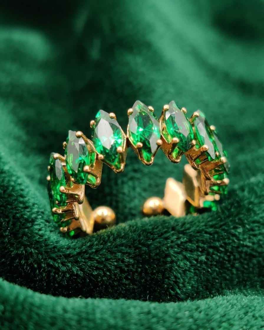 Close-up open crown ring with emerald-green stones on a gold-tone band