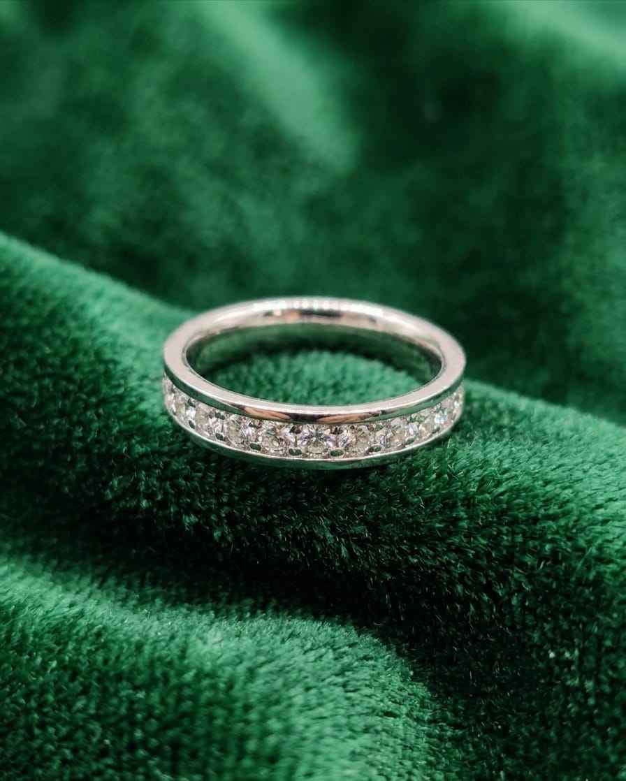 Silver eternity band with small clear stones, resting on green fabric