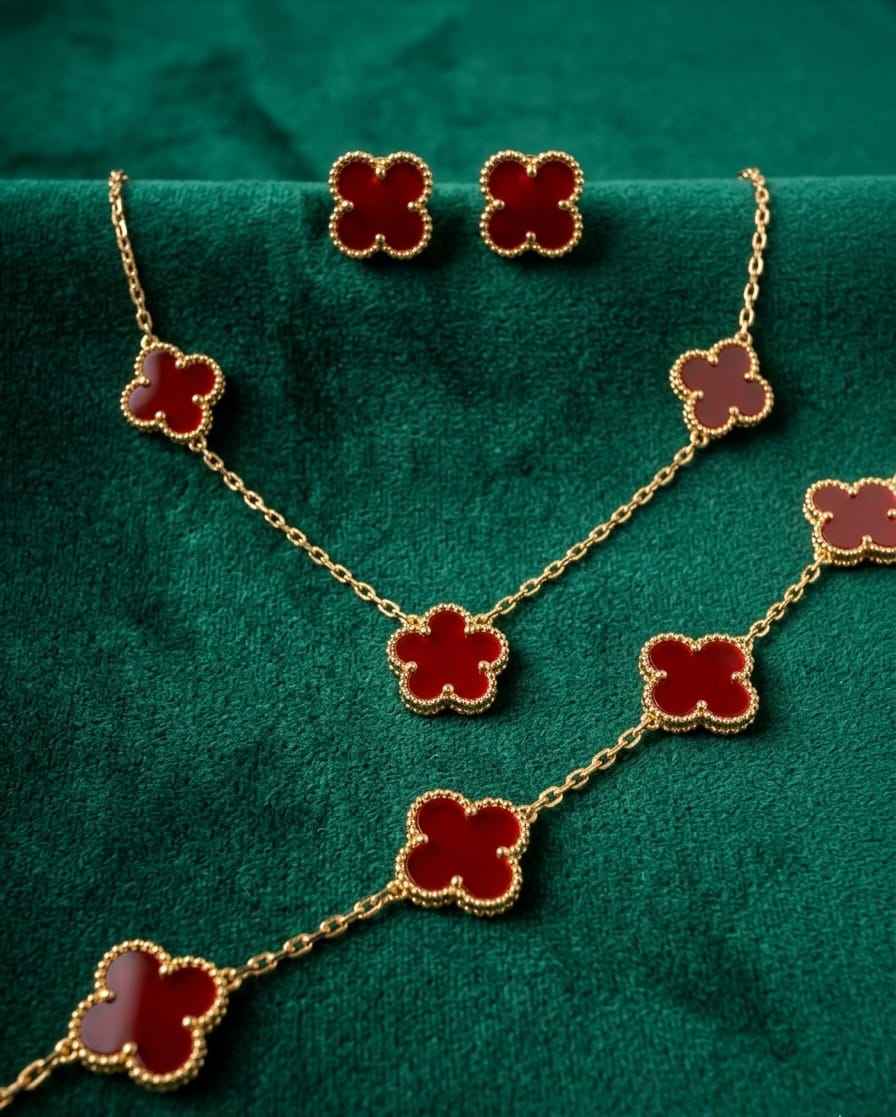 Gold-tone red clover charm necklace and bracelet set on green fabric