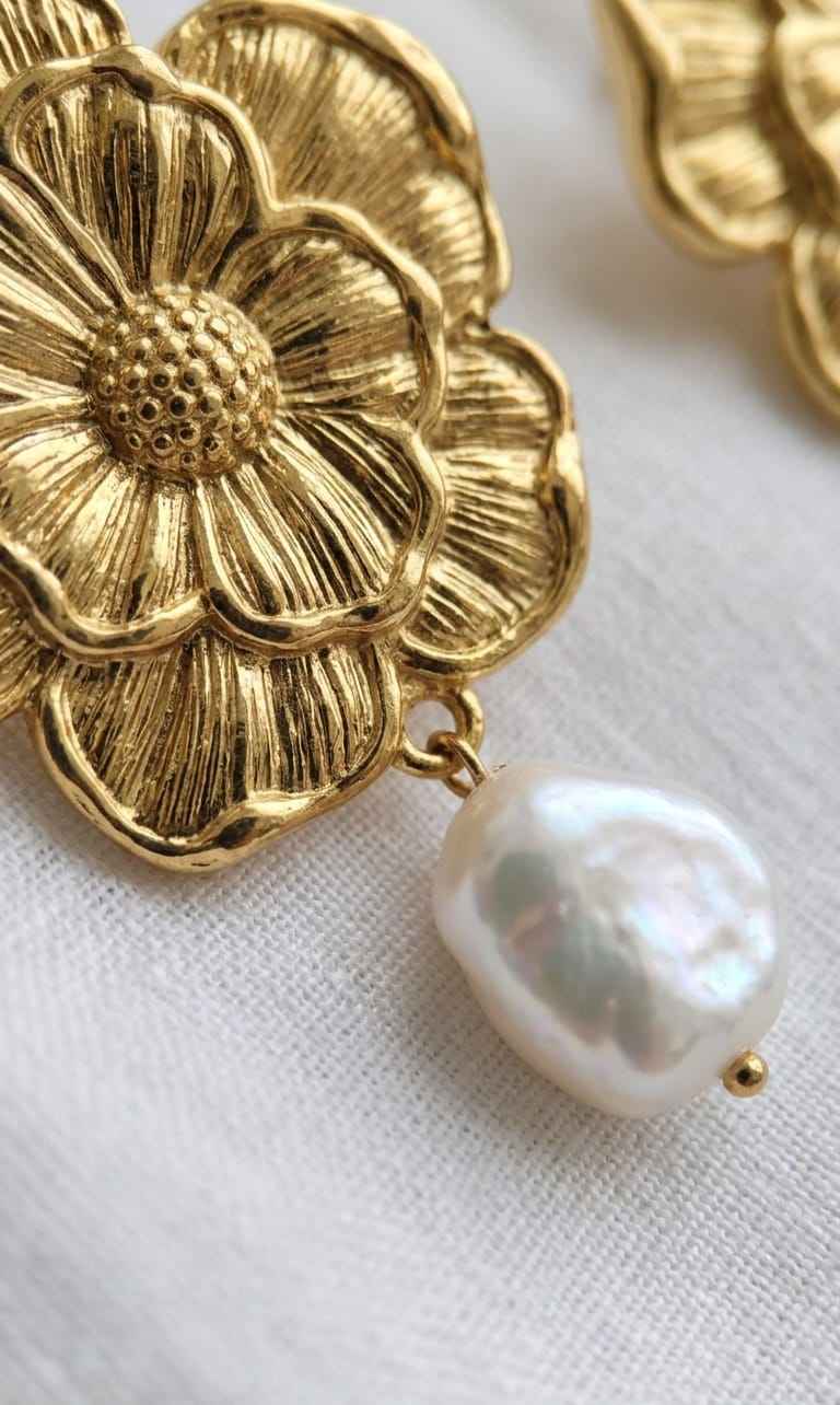 Gold flower earrings with white pearl drop dangles, close-up detail