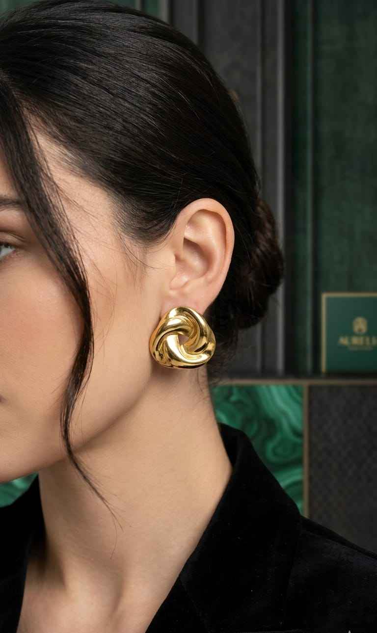 Gold twisted knot stud earrings worn on the ear, glossy swirl knot